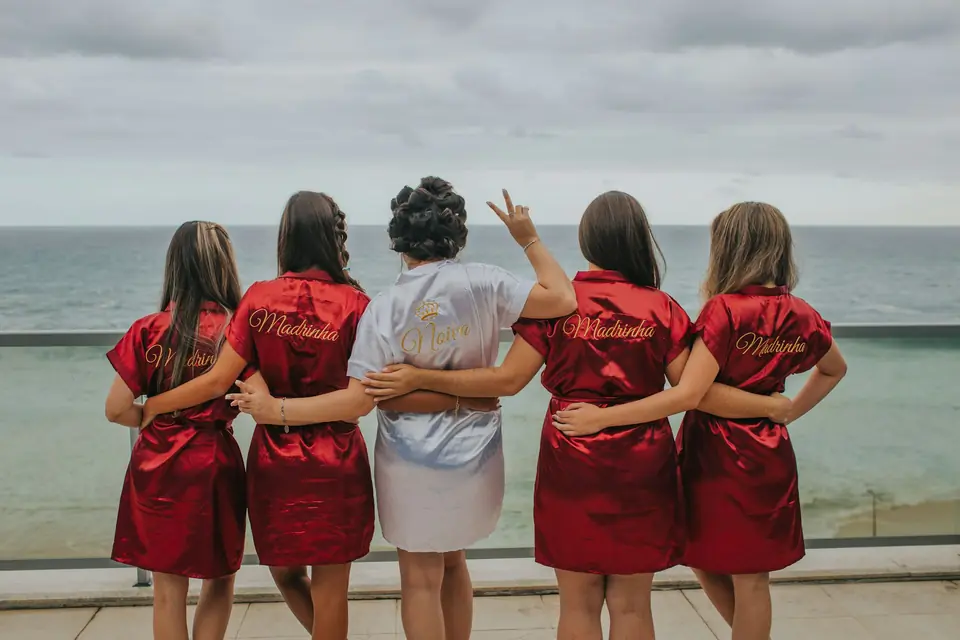 Friends in matching red robes with arms around each other by the sea