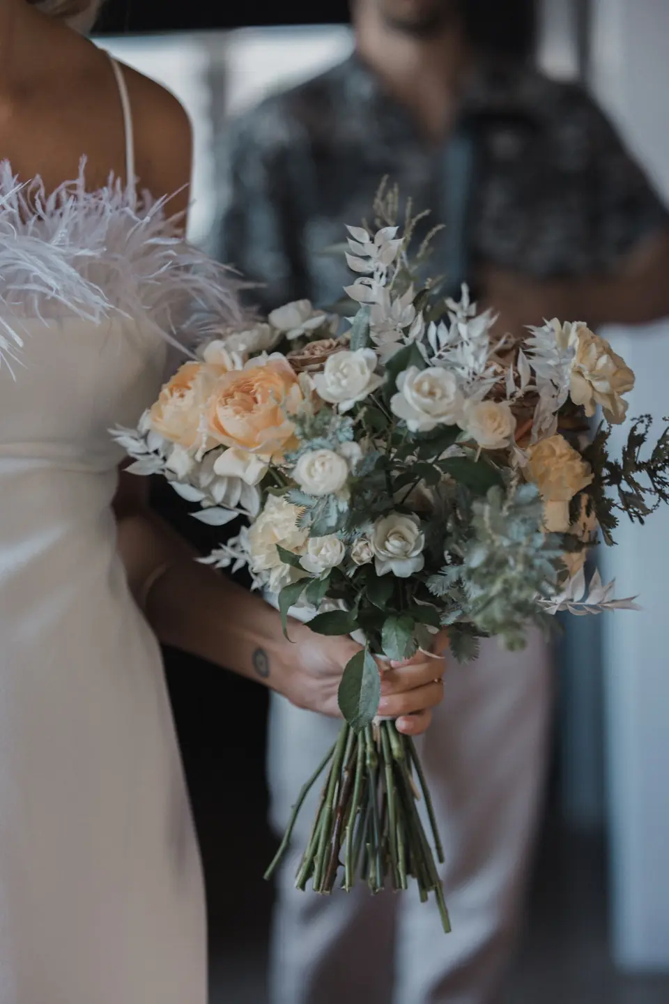 A peach and white garden bouquet held between the couple