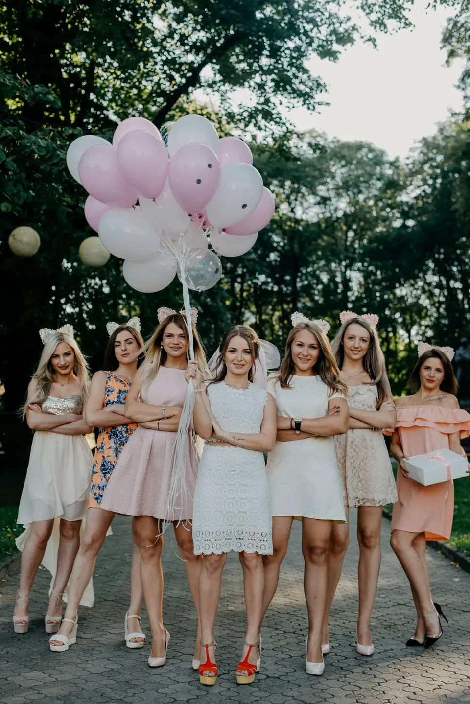 A bride-to-be and her friends in white holding pink balloons