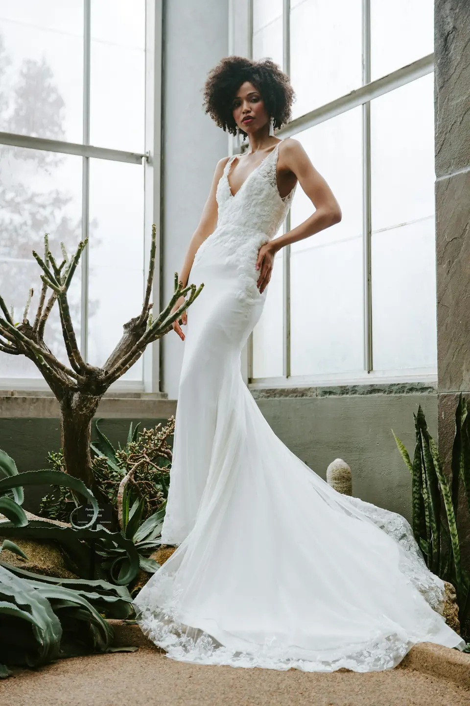 A bride in a fitted mermaid dress with a long train by tall windows