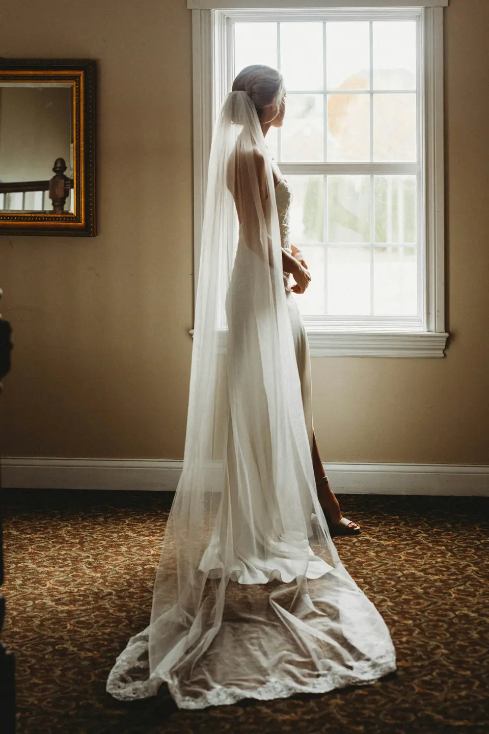 A bride by a window with a long veil pooling on the floor