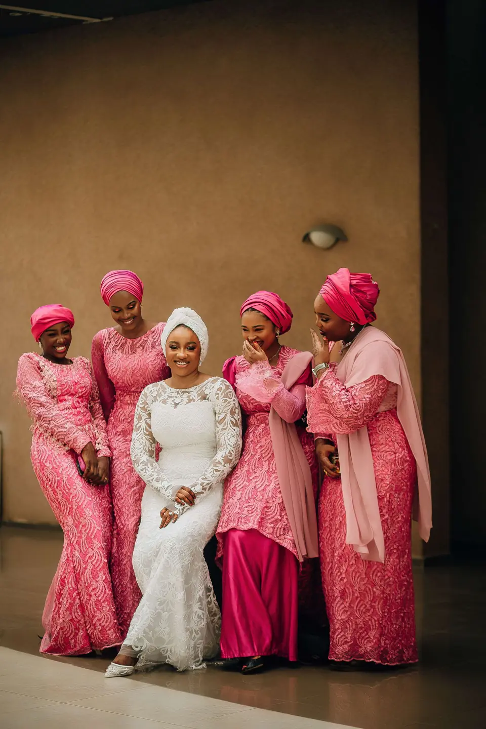 A bride with her bridesmaids in pink dresses and matching gele head wraps