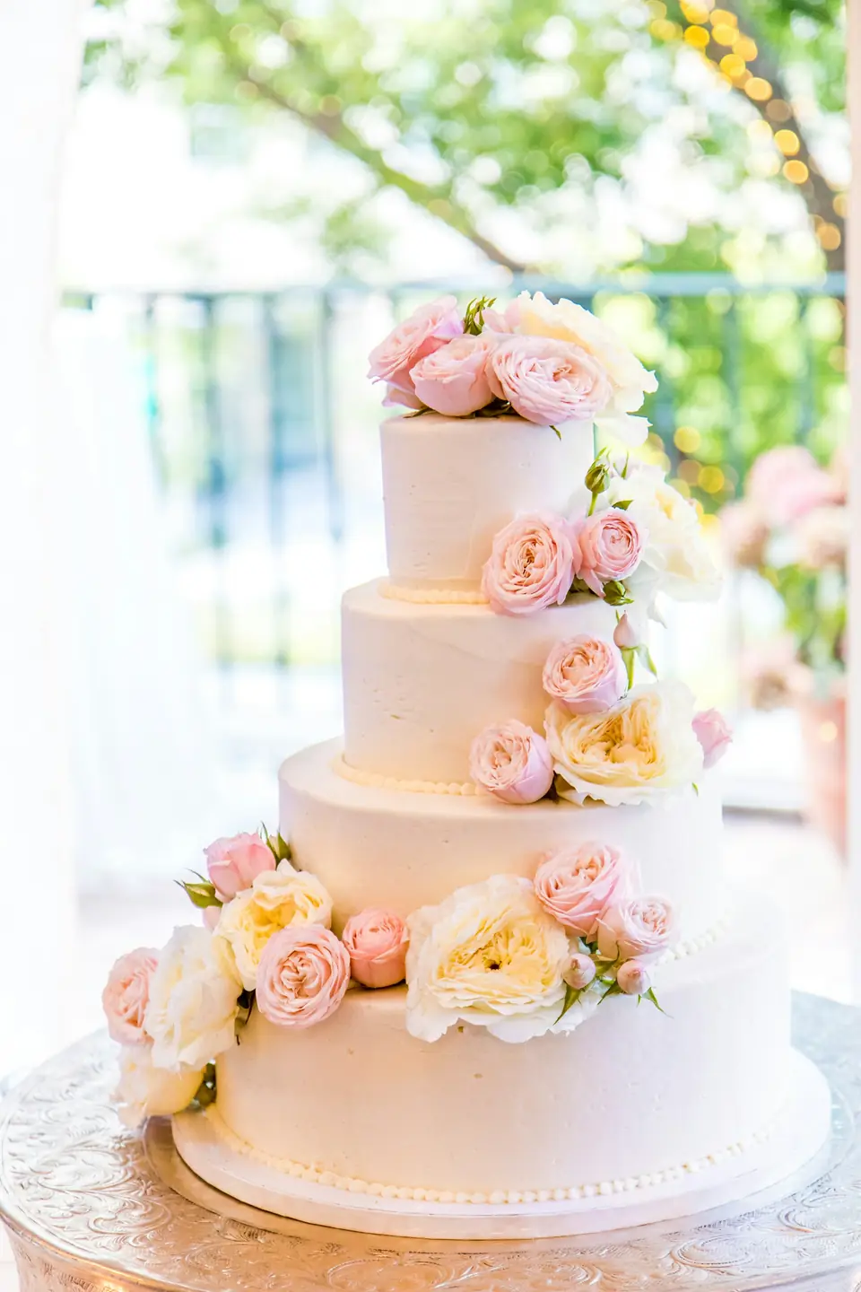 A four-tier white wedding cake decorated with peach roses