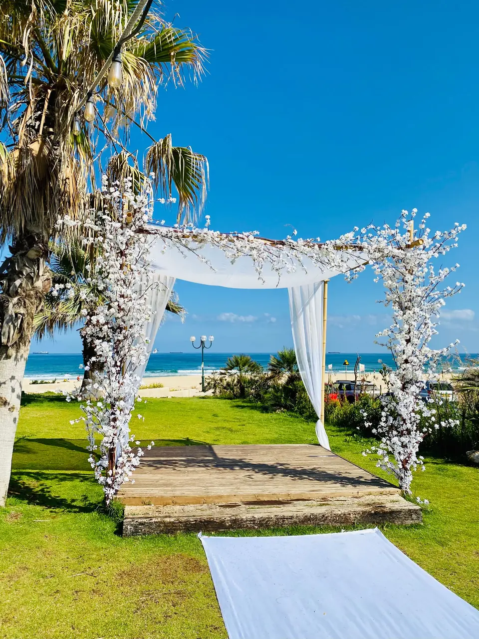 A four-post floral wedding canopy on a lawn above the sea
