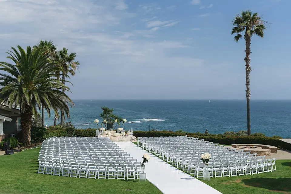 Rows of white chairs on a lawn above the ocean for a ceremony