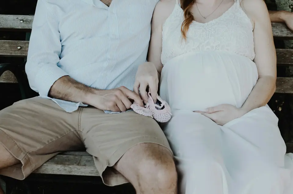 An expecting couple on a bench holding a tiny pair of baby shoes