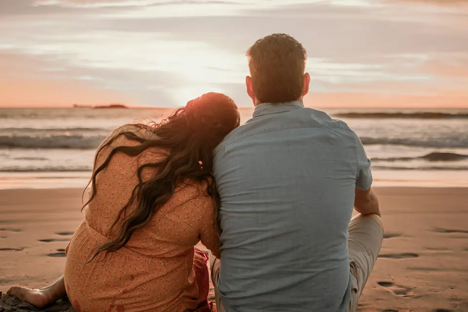 A couple sitting close together on a beach at sunset