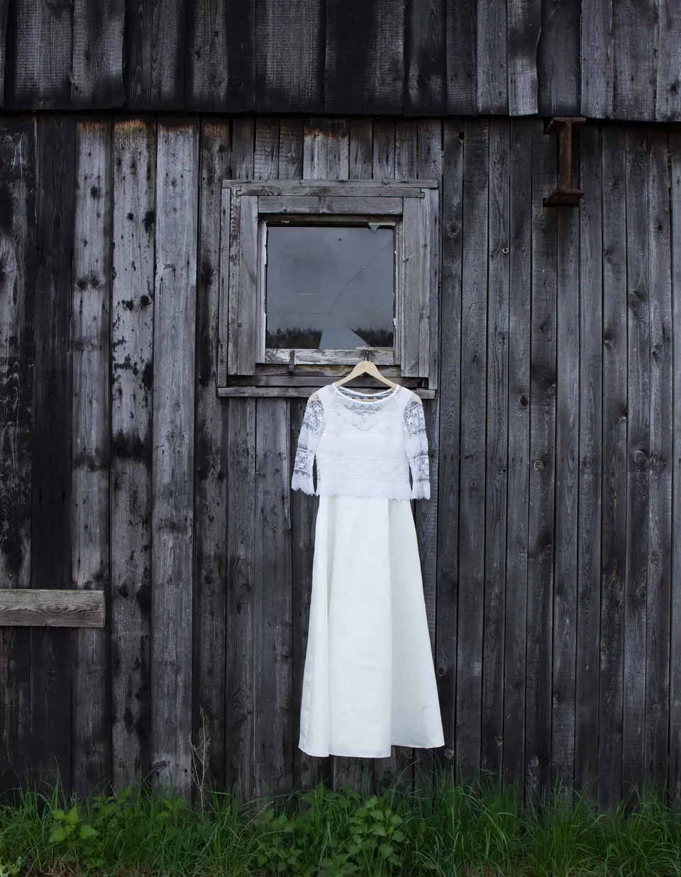 A wedding dress hanging on the weathered wall of a barn