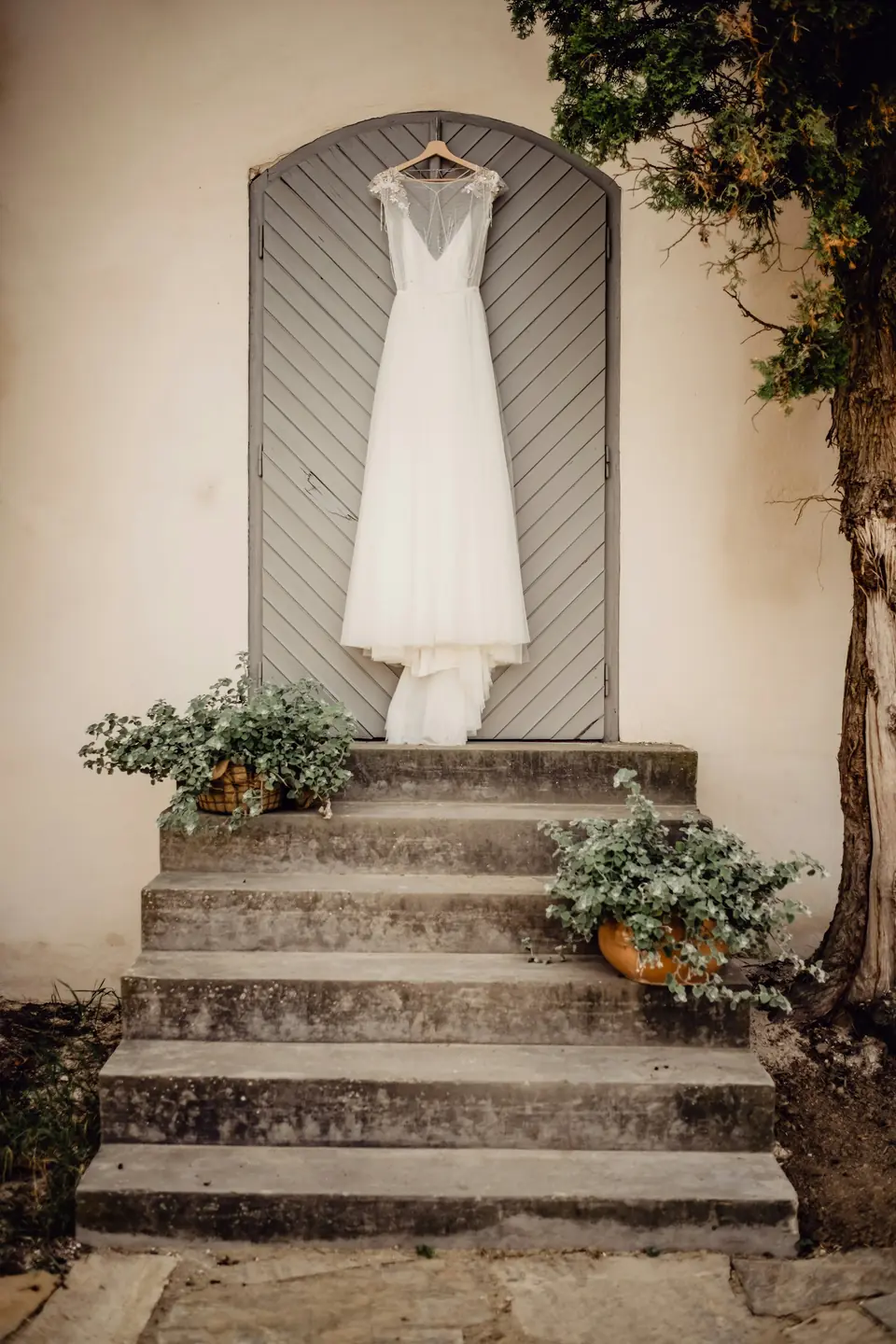A wedding dress hanging in an archway above stone steps and potted plants
