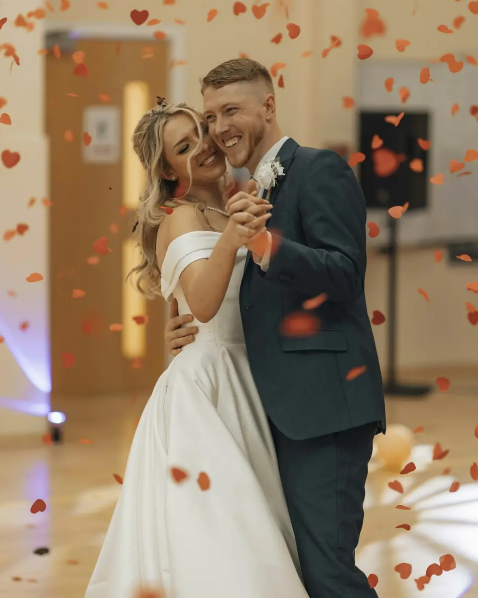 A laughing couple sharing their first dance as petals fall around them