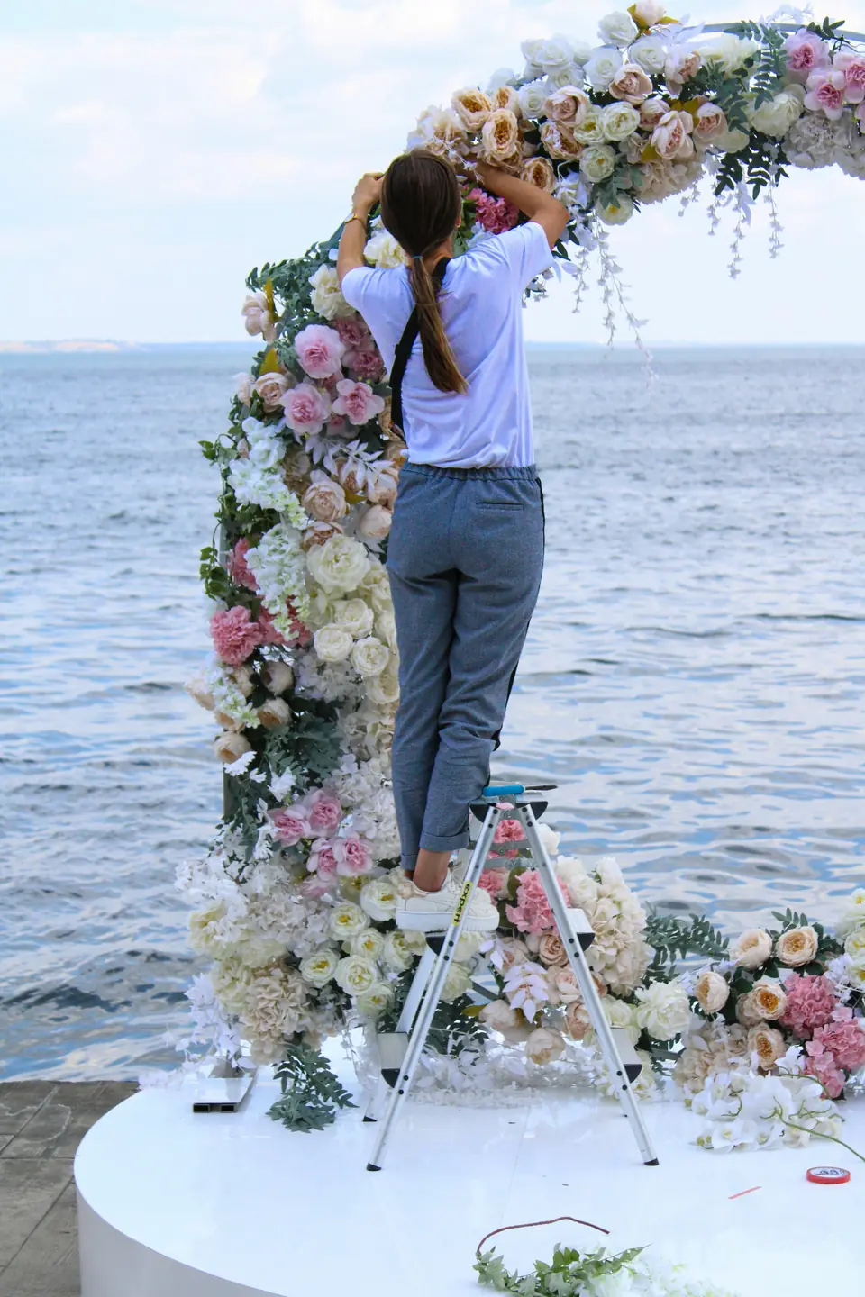 A florist finishing a round floral arch beside the sea