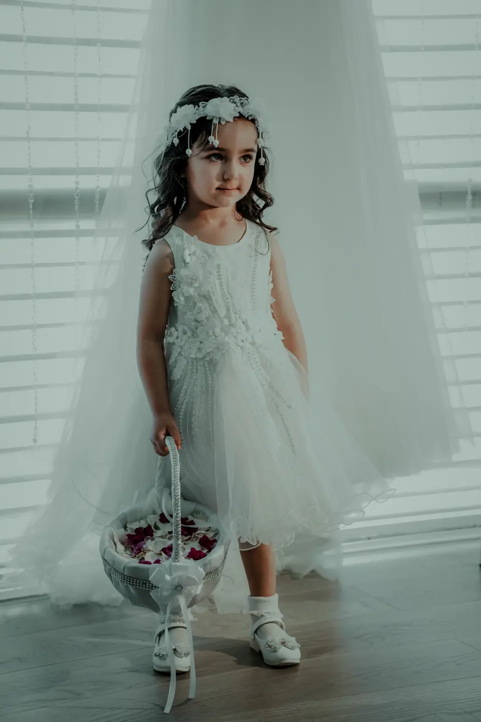A little flower girl in a white dress and flower crown holding a basket