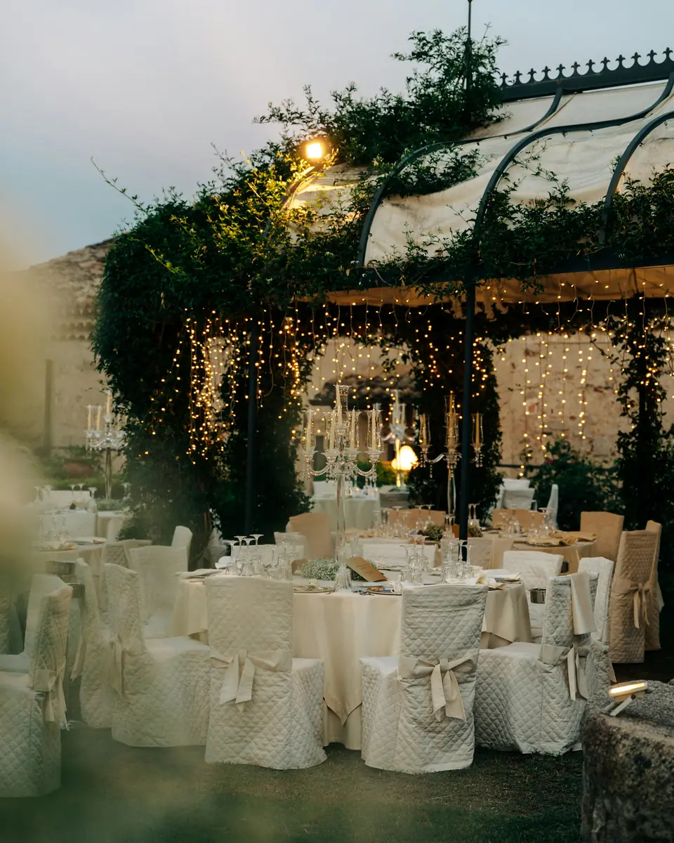 A reception set inside a glasshouse wrapped in greenery and lights