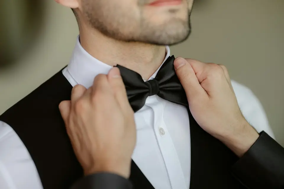 Hands straightening a groom's black bow tie