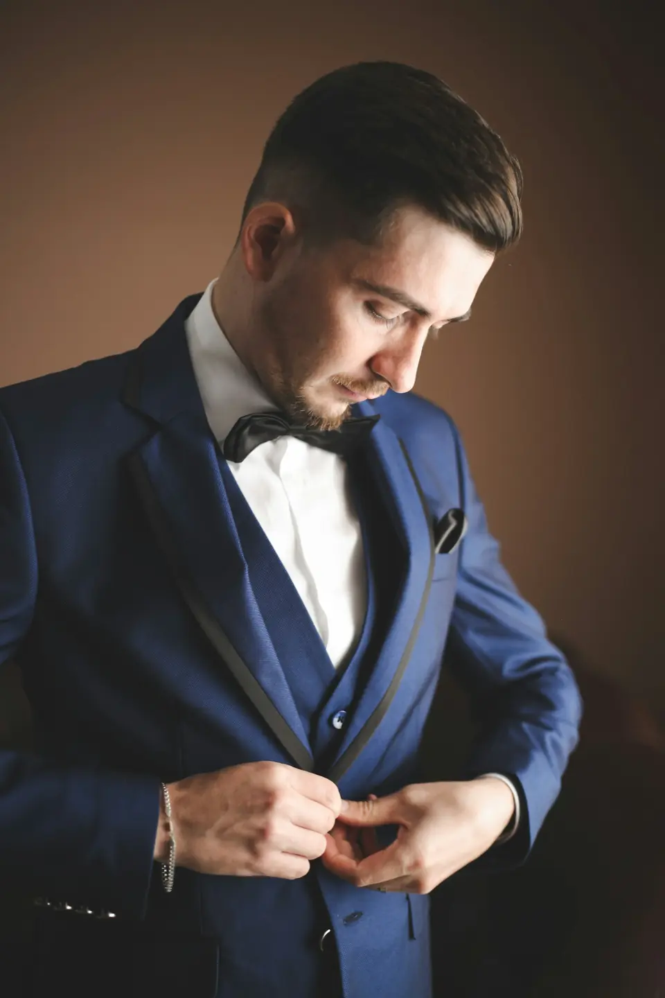 A groom in a navy three-piece suit fastening his jacket