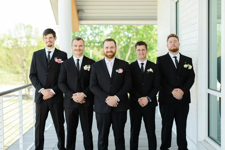 A groom and groomsmen in black suits standing in a row on a porch