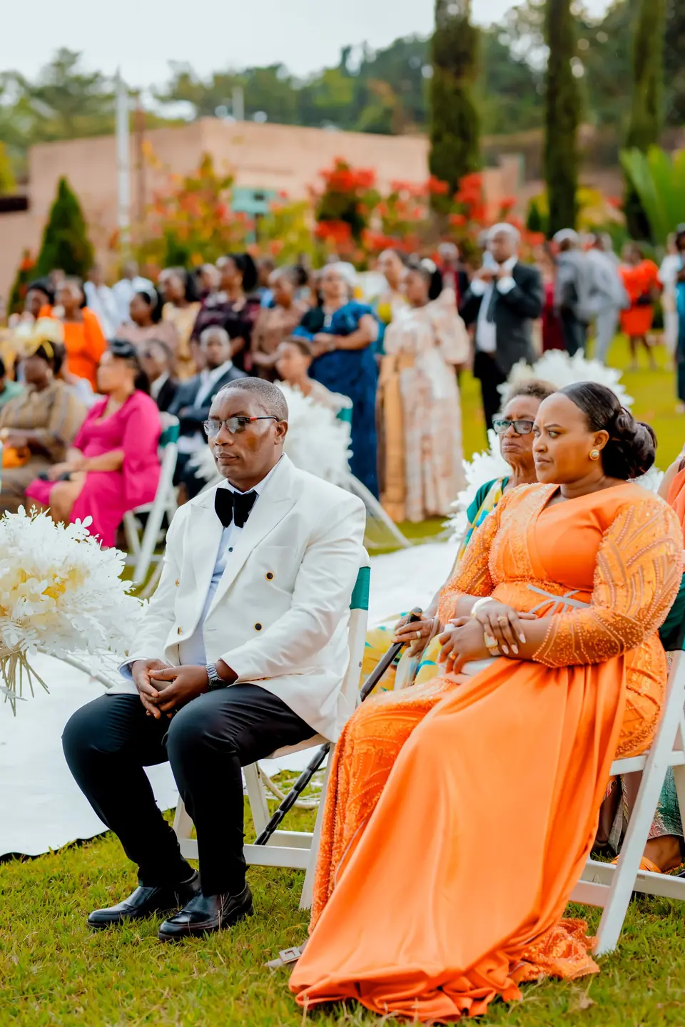Guests in a white suit and a bright orange dress seated at an outdoor wedding