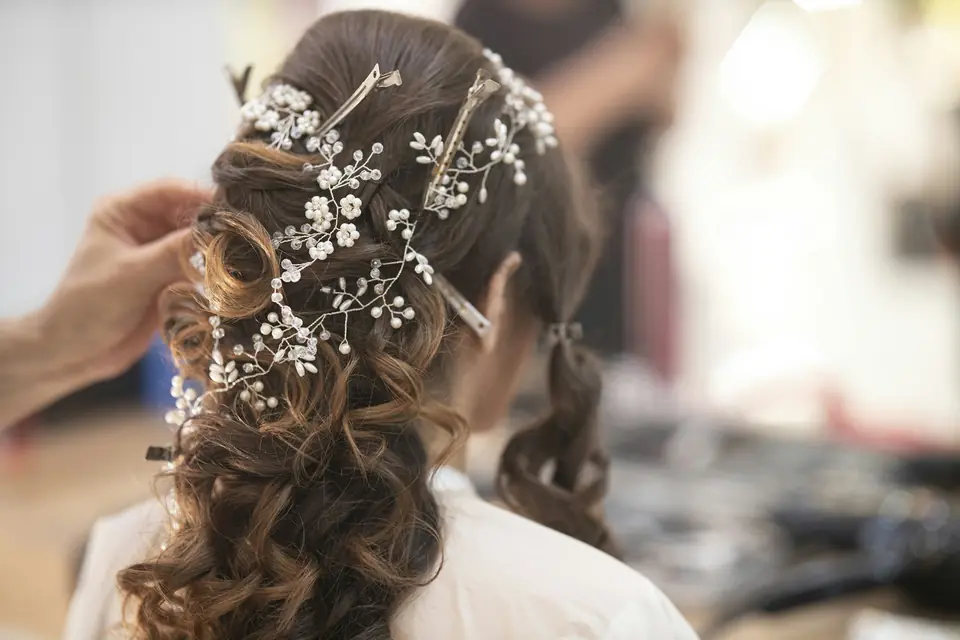 A hairstylist pinning a jeweled hairpiece into a bride's curls
