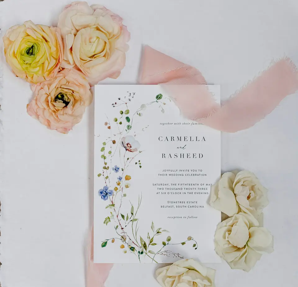 A watercolor floral wedding invitation surrounded by fresh flowers