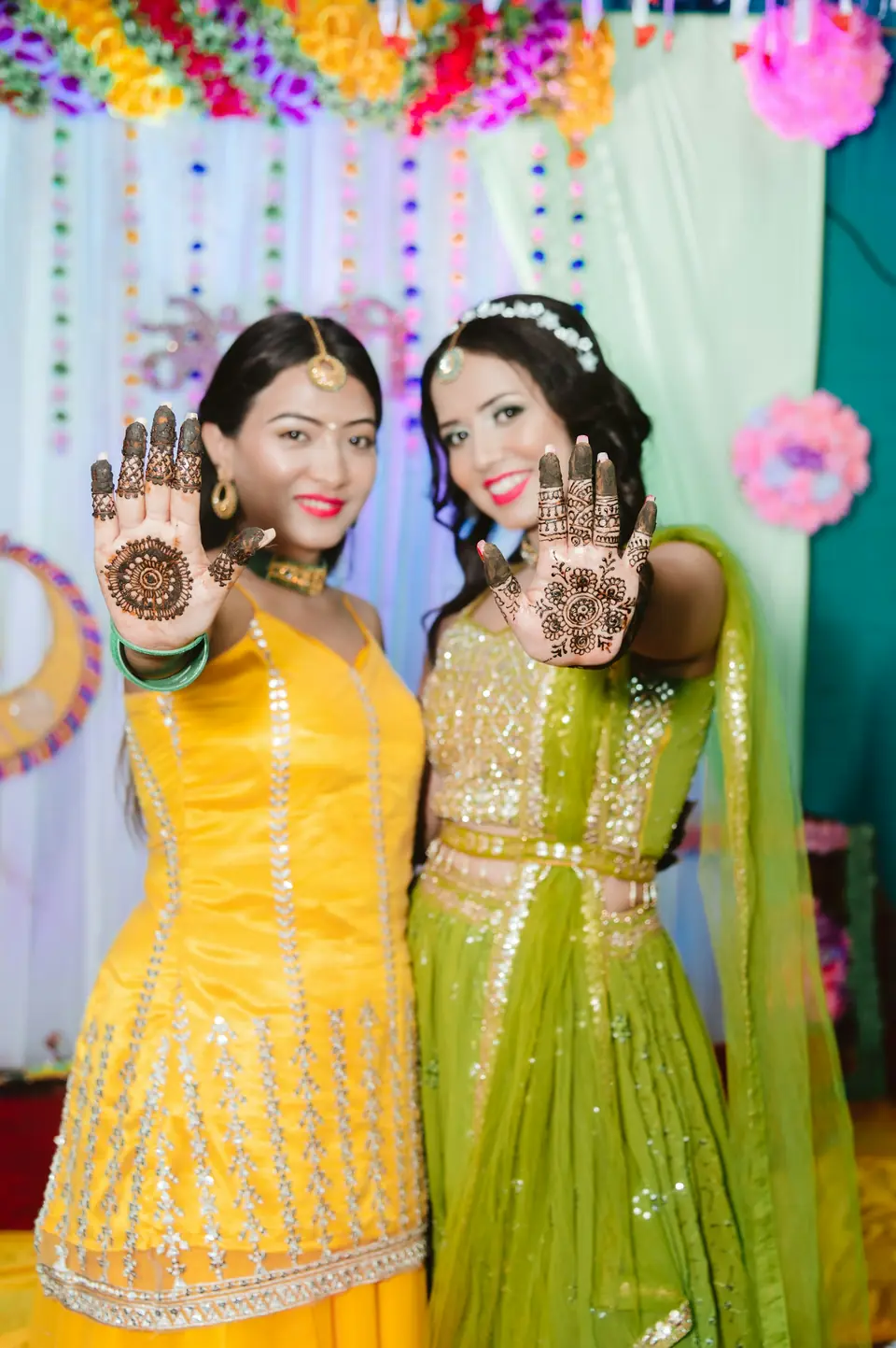 Two friends in yellow and green showing their mehndi