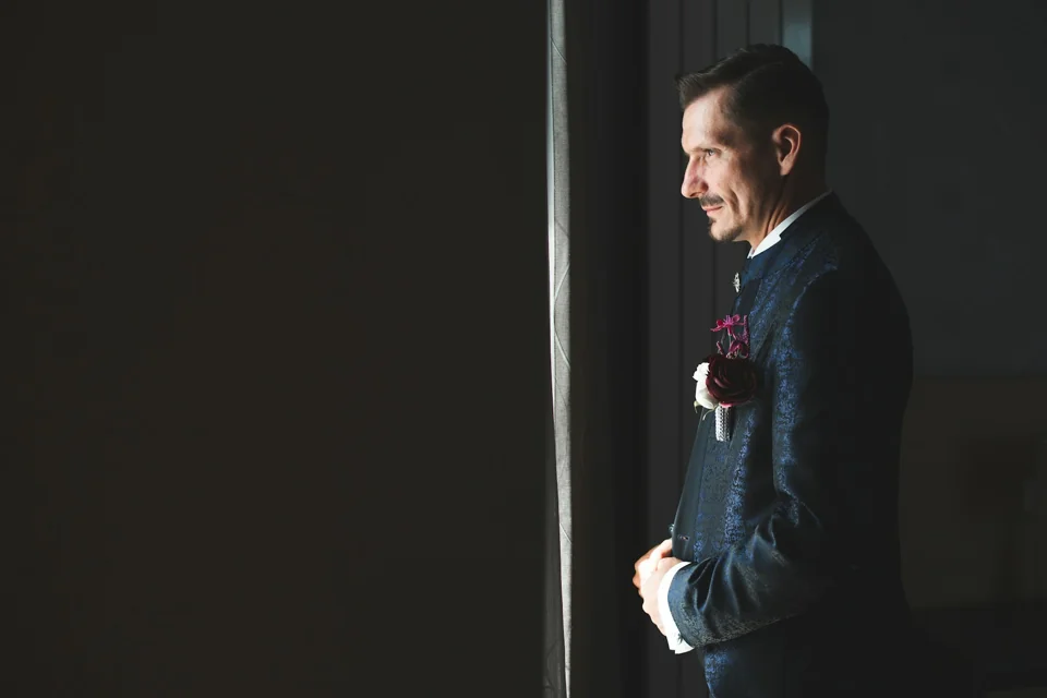 A groom in a suit beside a window