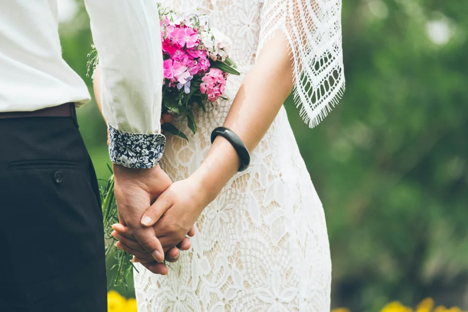 A couple holding hands beside a bridal bouquet