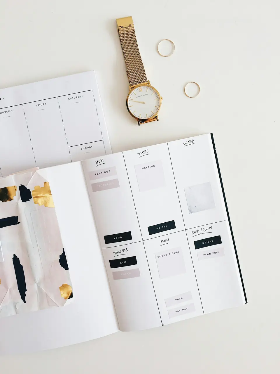A wedding planner notebook open beside a watch and small rings