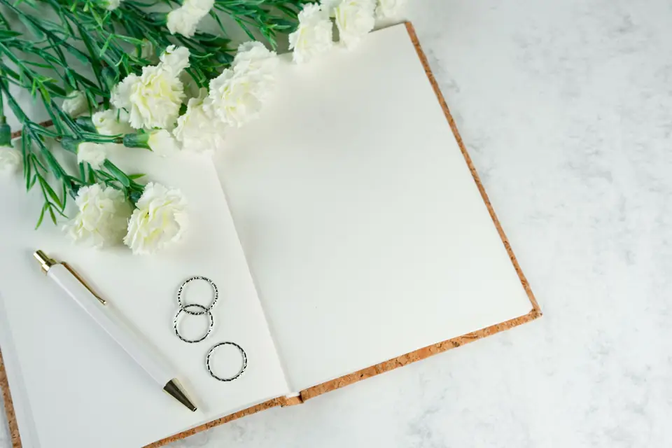 An open notebook with a pen, rings and white flowers on a marble table