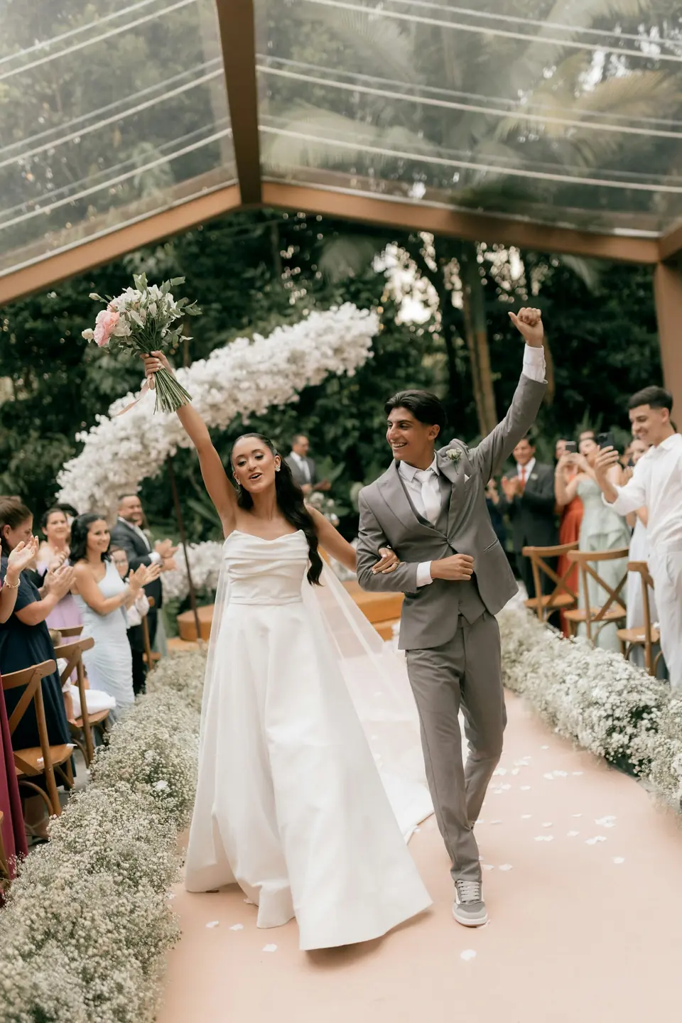 A bride and groom raising their arms in celebration as they walk back up the aisle
