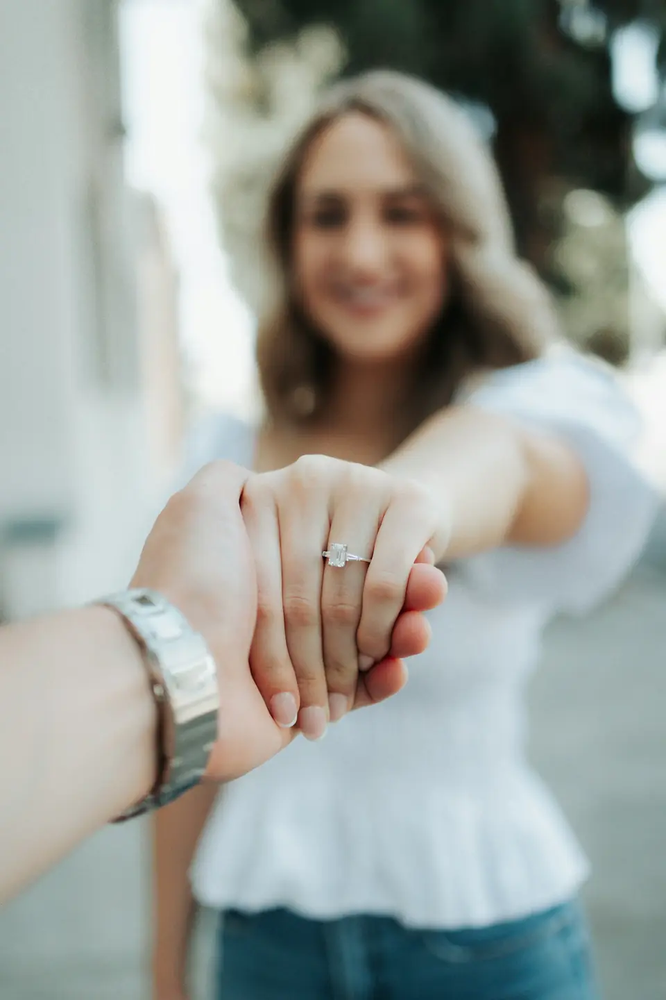 A smiling woman holding out her hand to show her engagement ring