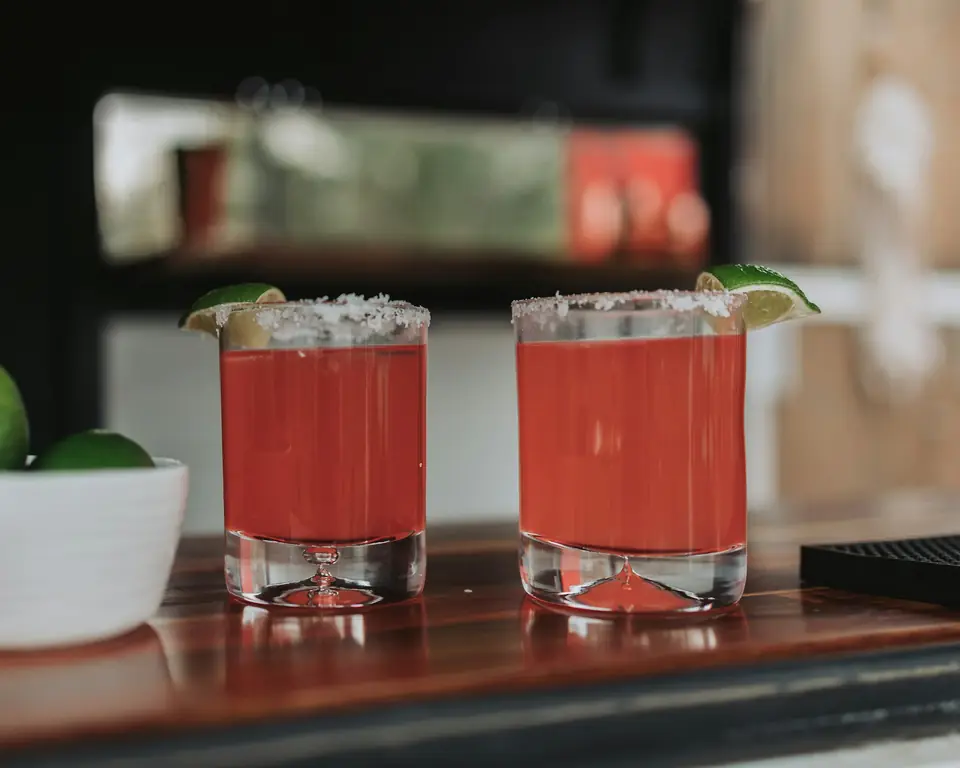 Two bright red signature cocktails with lime on a bar