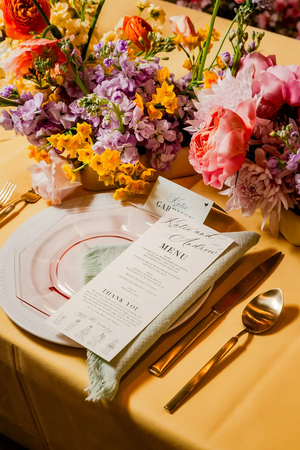 A place setting with a menu card beneath bright summer flowers